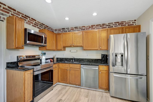 kitchen featuring light wood-type flooring, dark stone countertops, stainless steel appliances, sink, and brick wall