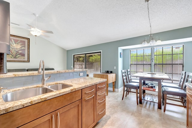 kitchen featuring hanging light fixtures, sink, vaulted ceiling, light stone counters, and a textured ceiling