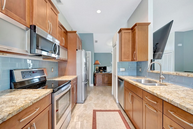 kitchen with appliances with stainless steel finishes, light stone countertops, sink, and backsplash