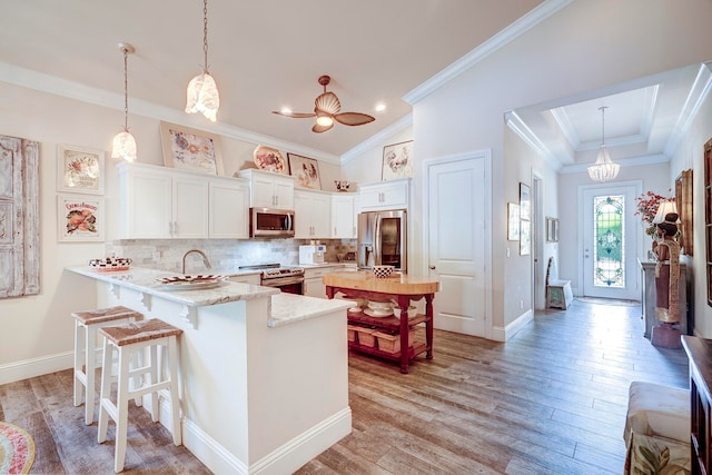 kitchen featuring kitchen peninsula, white cabinetry, stainless steel appliances, decorative light fixtures, and light hardwood / wood-style flooring