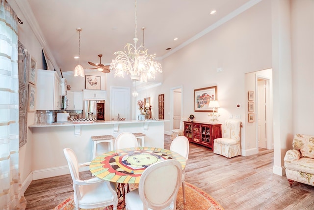 dining area featuring ornamental molding, a high ceiling, light wood-type flooring, and ceiling fan with notable chandelier