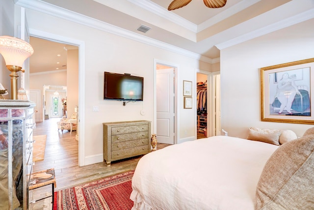 bedroom with light hardwood / wood-style floors, crown molding, ceiling fan, and a walk in closet