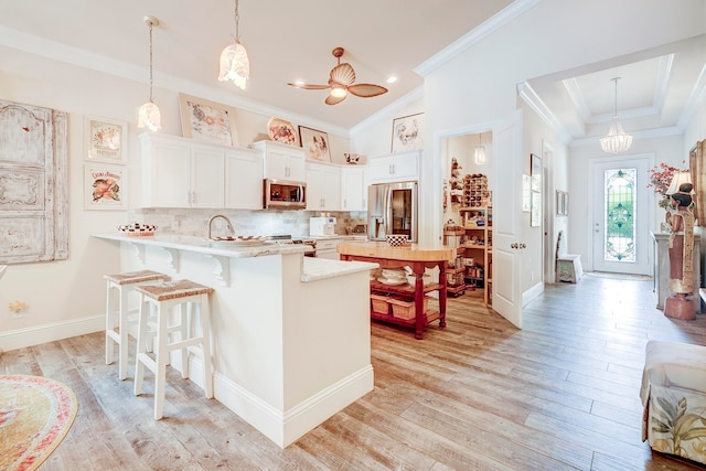 kitchen featuring kitchen peninsula, stainless steel appliances, pendant lighting, light wood-type flooring, and white cabinetry