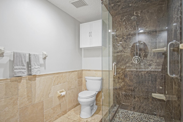 bathroom with a shower with door, a textured ceiling, tile walls, toilet, and tile patterned flooring