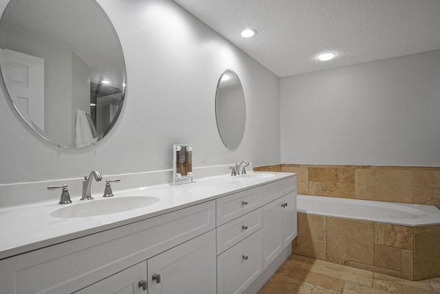 bathroom with vanity, a textured ceiling, and tiled tub