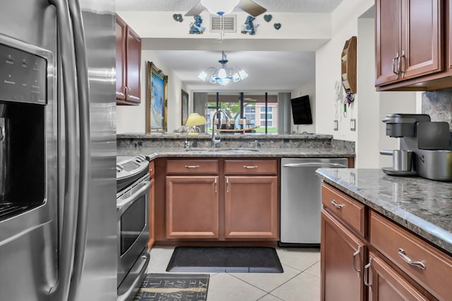 kitchen featuring sink, appliances with stainless steel finishes, an inviting chandelier, light tile patterned flooring, and dark stone counters