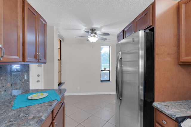 kitchen with light tile patterned flooring, tasteful backsplash, stainless steel fridge, stone counters, and ceiling fan