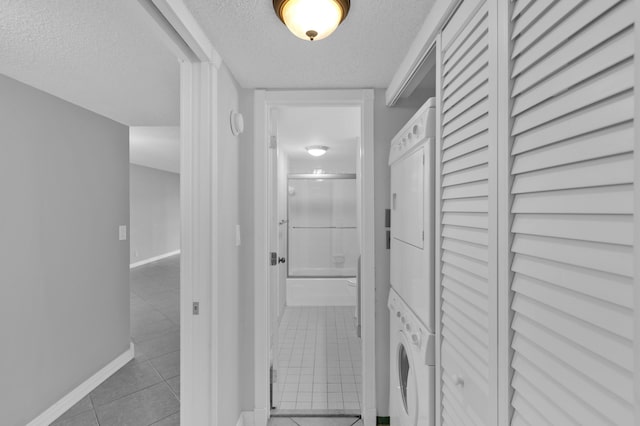 hallway with light tile patterned flooring, stacked washer and clothes dryer, and a textured ceiling