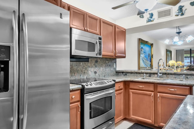 kitchen with ceiling fan with notable chandelier, sink, backsplash, light stone counters, and stainless steel appliances