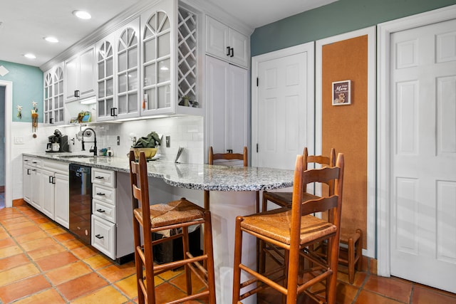 kitchen featuring dishwasher, backsplash, sink, light stone countertops, and a kitchen bar