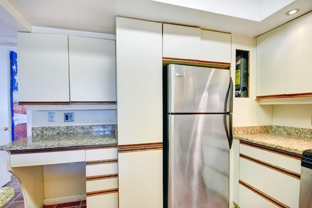 kitchen with light stone countertops, stainless steel fridge, white cabinets, and tile patterned flooring