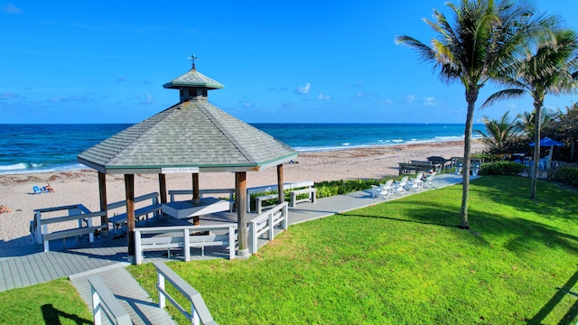 view of community featuring a lawn, a gazebo, a water view, and a beach view