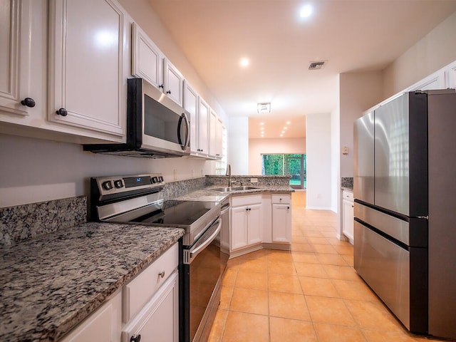 kitchen with appliances with stainless steel finishes, light tile patterned flooring, sink, white cabinets, and light stone counters