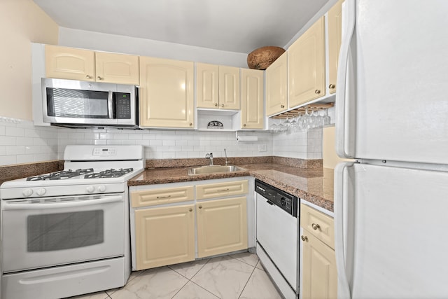 kitchen with tasteful backsplash, dark stone countertops, cream cabinetry, sink, and white appliances