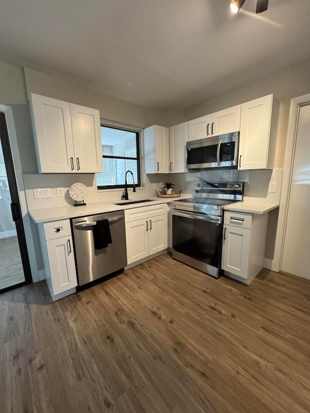 kitchen with dark wood-type flooring, stainless steel appliances, backsplash, sink, and white cabinetry