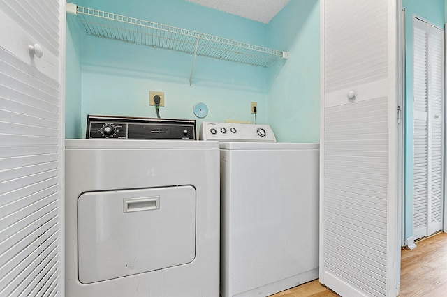 washroom with a textured ceiling, washing machine and clothes dryer, and light wood-type flooring