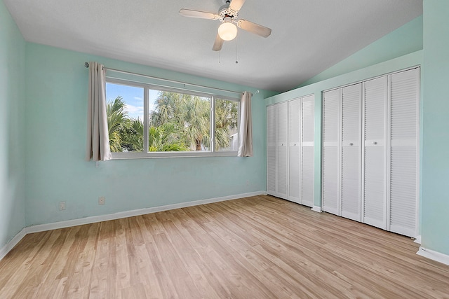 unfurnished bedroom featuring ceiling fan, multiple closets, vaulted ceiling, and light wood-type flooring