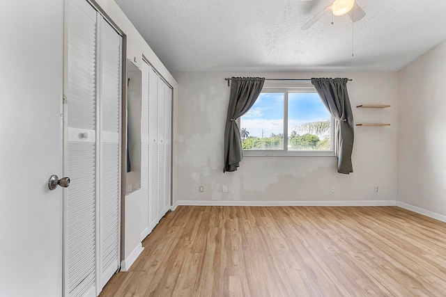 unfurnished bedroom with ceiling fan, multiple closets, a textured ceiling, and light wood-type flooring