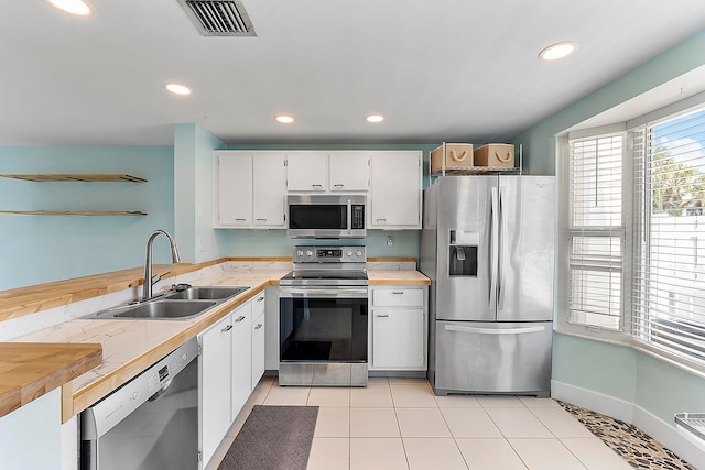 kitchen with stainless steel appliances, sink, light tile patterned flooring, and white cabinets