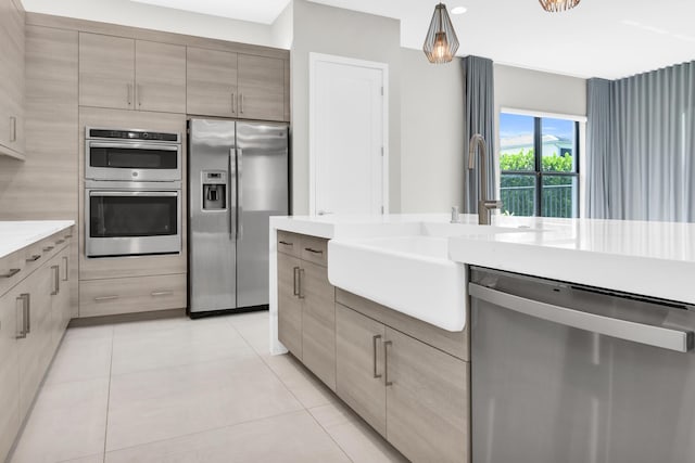 kitchen featuring stainless steel appliances, sink, light brown cabinets, light tile patterned floors, and decorative light fixtures