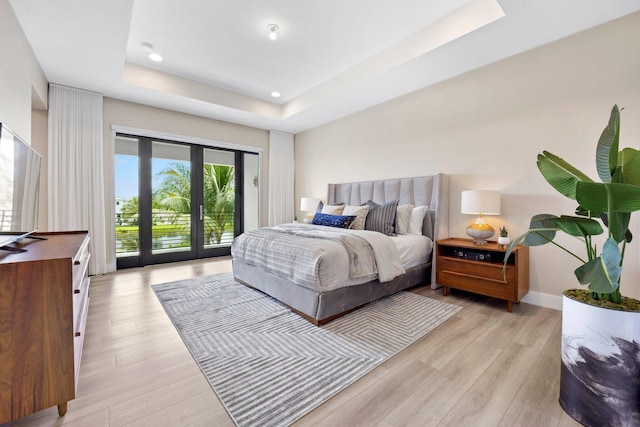 bedroom with a raised ceiling, light wood-type flooring, and access to outside