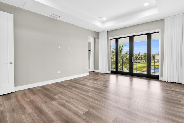 spare room with light hardwood / wood-style floors, a raised ceiling, and french doors