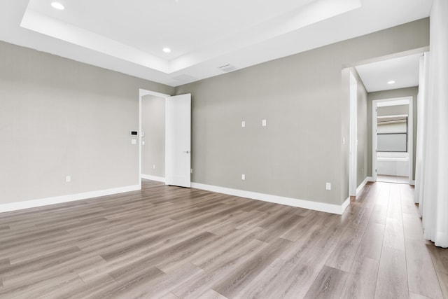 empty room with a raised ceiling and light hardwood / wood-style flooring