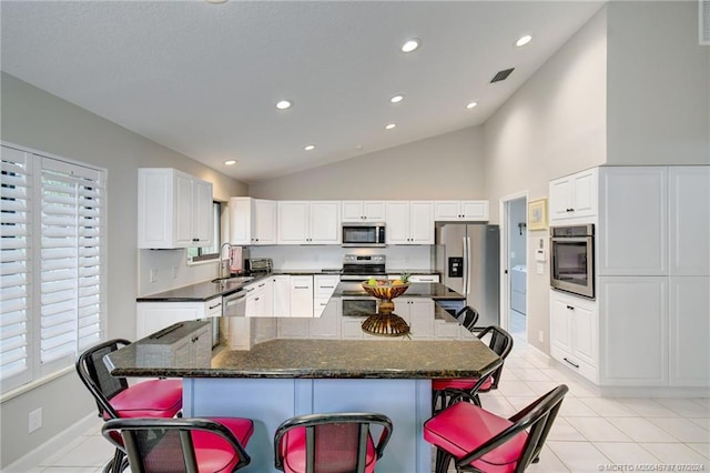 kitchen with white cabinetry, stainless steel appliances, a breakfast bar area, and vaulted ceiling