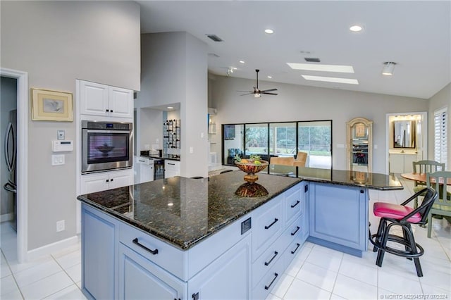 kitchen with dark stone counters, a kitchen island, vaulted ceiling with skylight, white cabinetry, and stainless steel oven