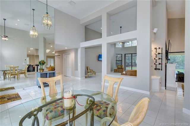 tiled dining space featuring a towering ceiling, ceiling fan with notable chandelier, and a healthy amount of sunlight