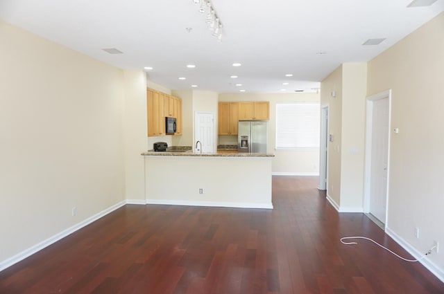 kitchen with light brown cabinetry, dark hardwood / wood-style flooring, kitchen peninsula, stainless steel fridge, and light stone counters