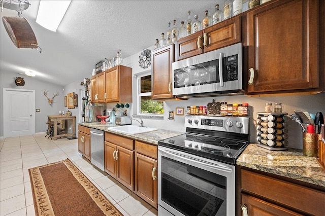 kitchen featuring sink, stone countertops, stainless steel appliances, lofted ceiling, and light tile patterned floors