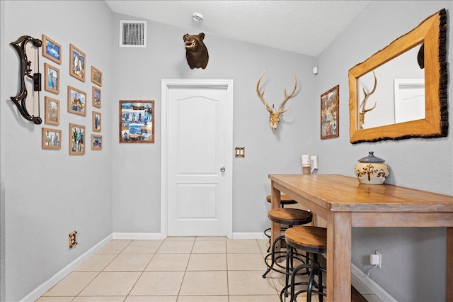 interior space featuring lofted ceiling, light tile patterned flooring, and a textured ceiling