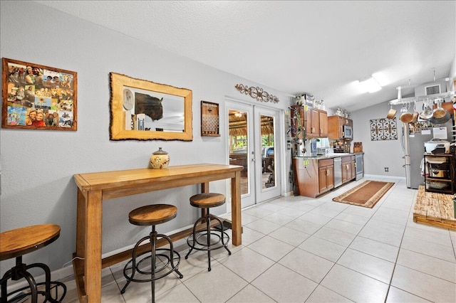 kitchen with french doors, stainless steel appliances, light tile patterned floors, and vaulted ceiling