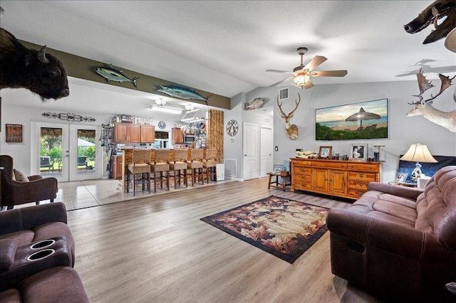 living room with french doors, ceiling fan, lofted ceiling, and light wood-type flooring