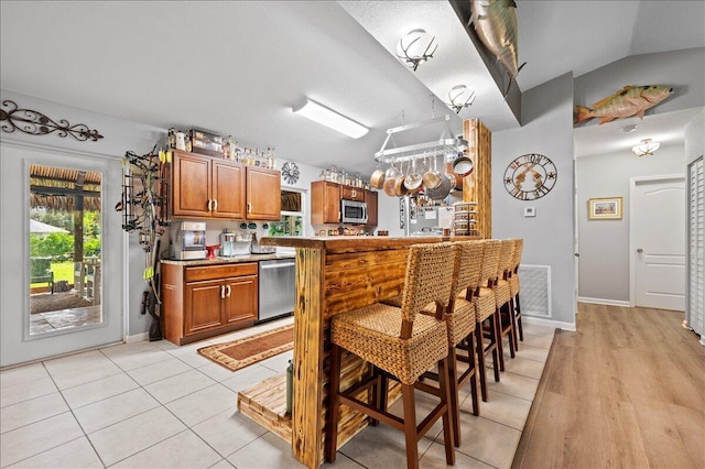 kitchen featuring vaulted ceiling, stainless steel appliances, and light hardwood / wood-style flooring