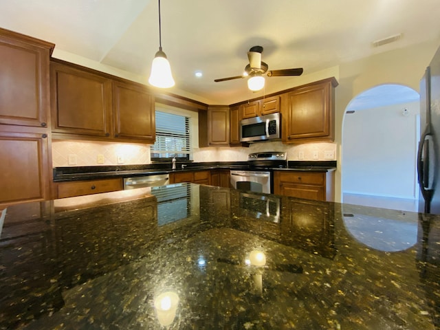 kitchen with pendant lighting, backsplash, stainless steel appliances, and dark stone counters