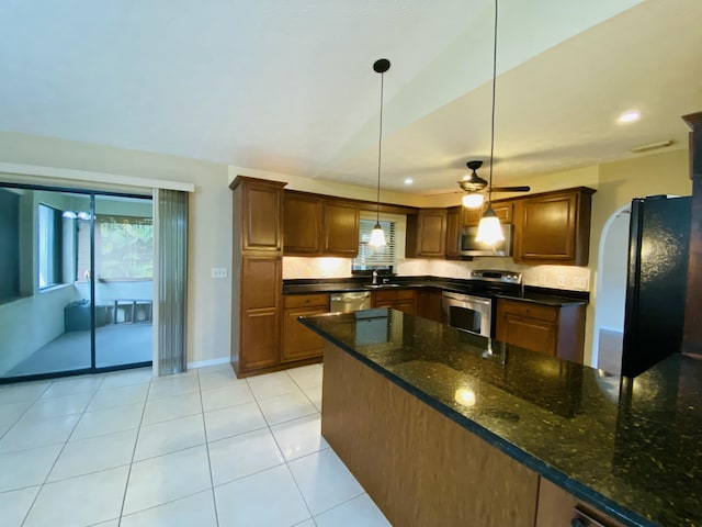 kitchen featuring appliances with stainless steel finishes, ceiling fan, light tile patterned floors, dark stone countertops, and hanging light fixtures