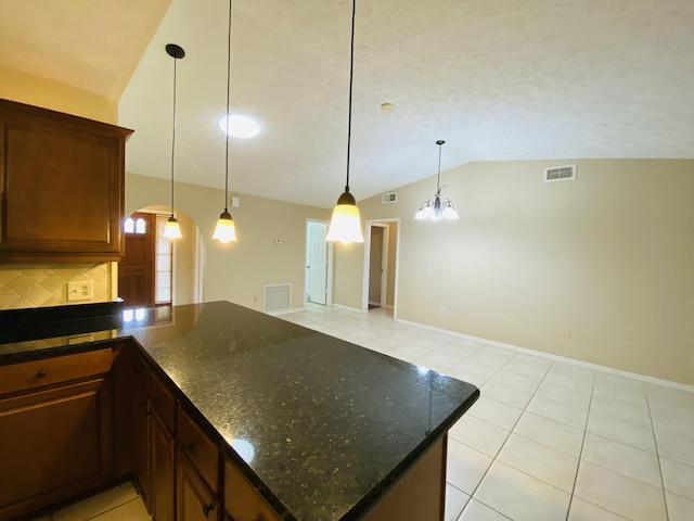 kitchen with pendant lighting, lofted ceiling, an inviting chandelier, light tile patterned floors, and tasteful backsplash