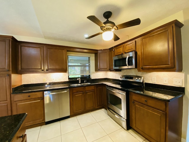 kitchen with stainless steel appliances, ceiling fan, sink, light tile patterned floors, and dark stone countertops