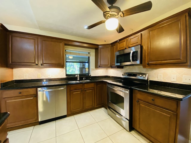 kitchen featuring appliances with stainless steel finishes, dark stone counters, ceiling fan, sink, and light tile patterned flooring