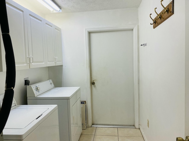 washroom with cabinets, light tile patterned floors, a textured ceiling, and washer and dryer