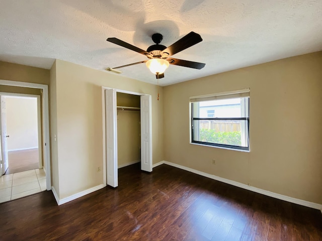 unfurnished bedroom featuring ceiling fan, a closet, dark wood-type flooring, and a textured ceiling