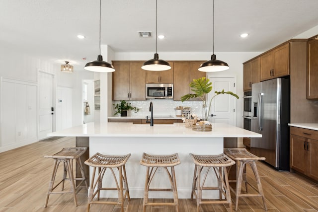 kitchen featuring hanging light fixtures, appliances with stainless steel finishes, light hardwood / wood-style flooring, and an island with sink