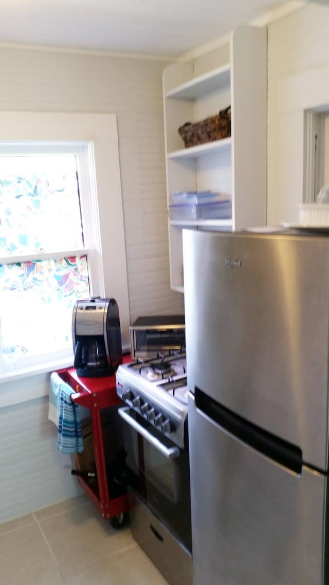 kitchen with gas range oven, light tile patterned floors, and stainless steel fridge