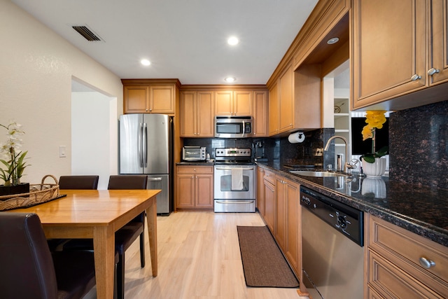 kitchen featuring sink, light wood-type flooring, backsplash, stainless steel appliances, and dark stone countertops