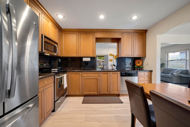 kitchen with a wealth of natural light, stainless steel appliances, light wood-type flooring, and dark stone counters