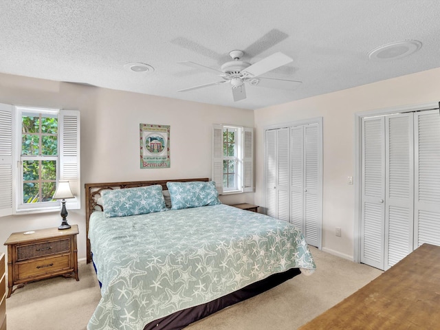 carpeted bedroom featuring a textured ceiling, multiple closets, and ceiling fan