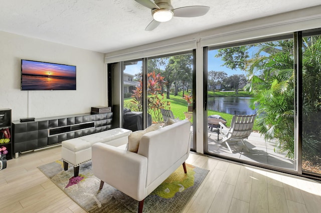 living room with a textured ceiling, ceiling fan, a water view, and light wood-type flooring