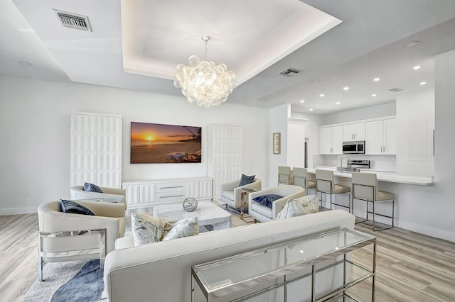 living room featuring a tray ceiling, a chandelier, and light wood-type flooring